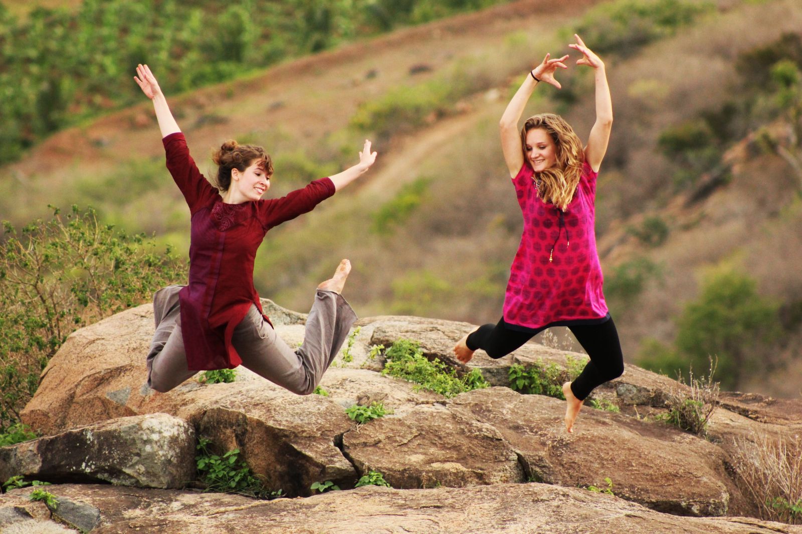 Zwei junge Frauen in indischen Gewändern springen in die Luft, im Hintergrund Felsen