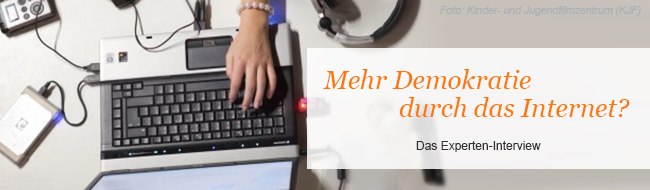 Bild zeigt von oben einen Laptop, Kopfhörer und ein paar Hände mit Schriftzug "Mehr Demokratie durch das Internet?"