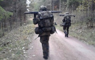 Zwei Soldaten in Camouflage laufen mit Rucksack und Gewehr über einen Feldweg