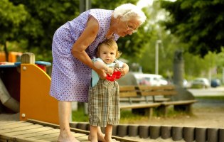 Foto: André Hirtz / www.jugendfotos.de Alte Frau hebt kleines Kind in Sandkasten