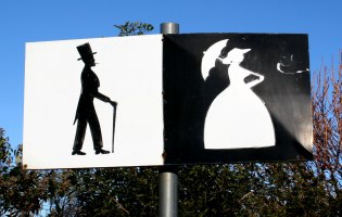 Schild mit Umrissen eines Mannes mit Zylinder, schwarz auf weiß, Frau mit Sonnenschirm, weiß auf schwarz