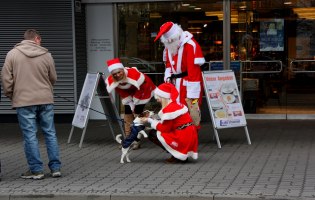 gynti_46 / www.flickr.com, CC-Lizenz (by-nc-sa) Hund an Leine wird von Frau in Weihnachtskostüm gestreichelt, weitere Weihnachtsfrau und Weihnachtsmann schauen zu