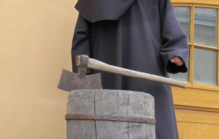 Henkeraxt auf einem Holzfass, dahinter in Kutte ein Henker