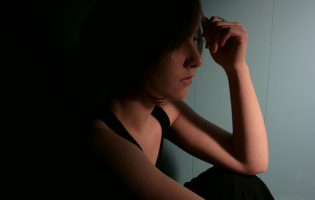 Junge Frau sitzt im Dunkeln, spielt mit ihren Haaren