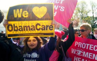 Junge Frau hält Plakat in die Höhe, auf dem steht: We love ObamaCare; im Hintergrund weitere Demonstrierende