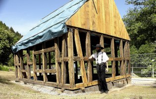 Foto: sharpals, flickr.com, CC-Lizenz (CC BY-NC-ND 2.0) Auf dem Foto ist ein Zimmermann vor einem Haus zu sehen.