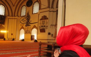 Auf dem Bild sieht man den in einem roten Tuch eingehüllten Hinterkopf von Yasemin. Sie betet in einer Moschee.