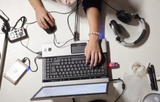 Auf dem Bild sind ein Laptop, Kopfhörer und zwei weibliche Hände zu sehen.