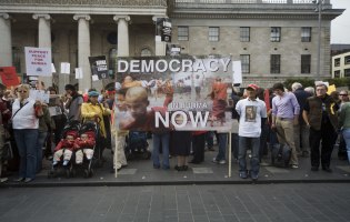 Eine Reihe von Menschen protestiert mit einem großen Plakat. Darauf steht "Democracy".