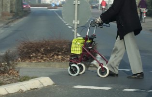 Eine ältere Person überquert mit dem Rollator die Straße
