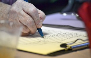 Hand einer älteren Person schreibt auf einen Block