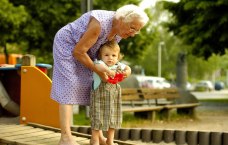 Alte Frau hebt kleines Kind in Sandkasten