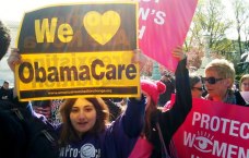 Junge Frau hält Plakat in die Höhe, auf dem steht: We love ObamaCare; im Hintergrund weitere Demonstrierende