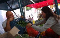 Auf dem Foto ist ein Mann auf einem Markt zu sehen, der einer Frau eine Kiste mit Bohnen überreicht.